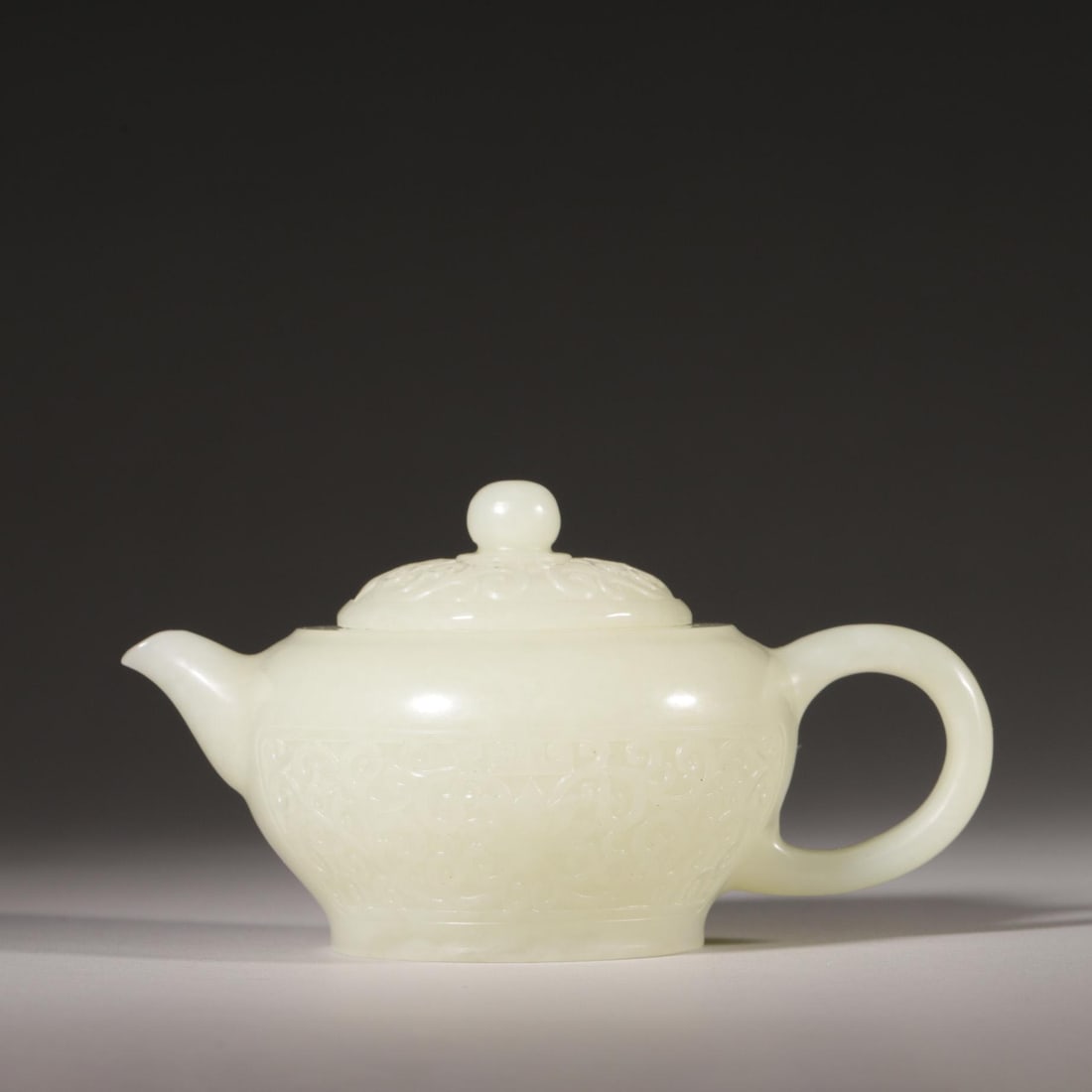 A Hetian White Jade Teapot with Scrolling Lotus Pattern, Qing Dynasty: L 13.5cm (5.31 in); W 9cm (3.54 in); H 8cm (3.15 in); Wt 232g (0.51 lb)A Qing Dynasty teapot carved from a single piece of Hetian white jade, with fine low-relief scrolling lotus patterns on the body 