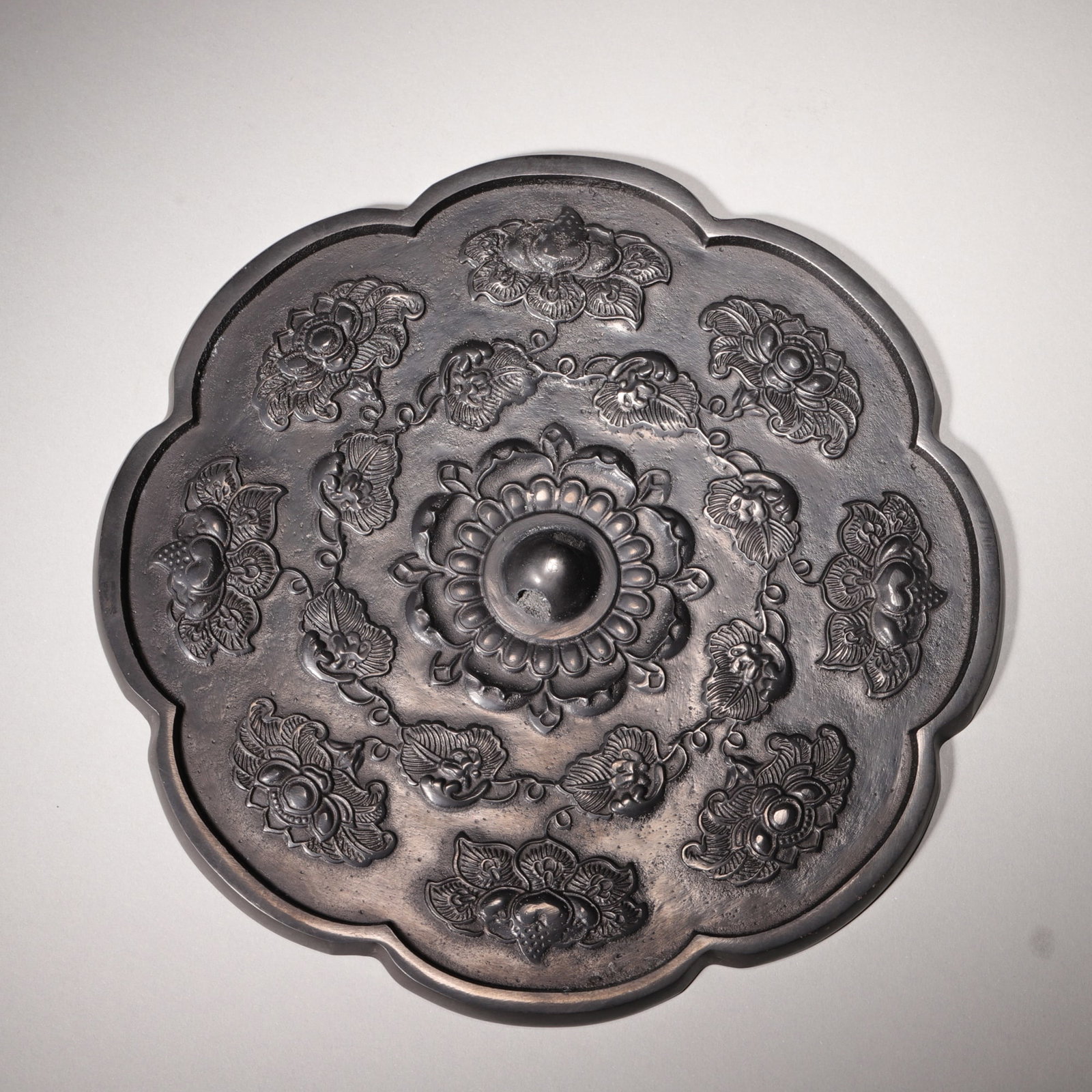 A BRONZE RHOMBUS MIRROR WITH FLORAL AND BAT MOTIFS, TANG DYNASTY: D 19.00cm (7.48 in); Wt 753.00g (1.66 lb),Eight-lobed rhombus bronze mirror with uniform black mercury patina. Central knob encircled by multi-layer precious floral reliefs. Intertwined vines connect 