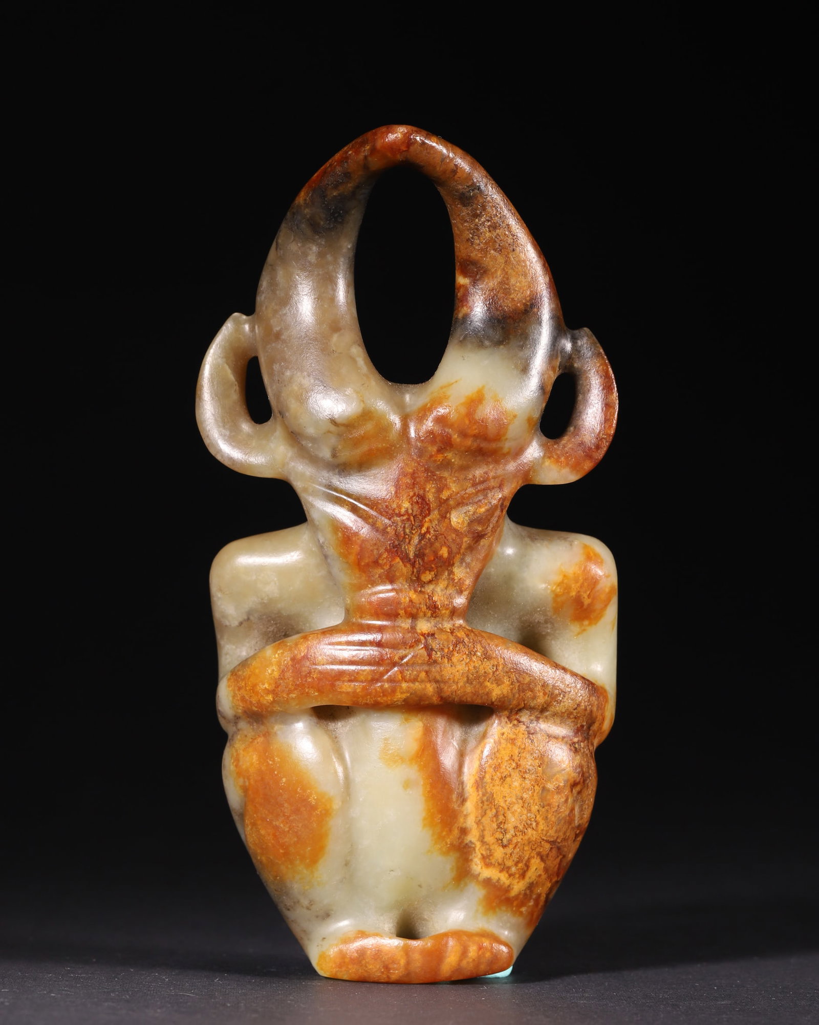 A Hongshan Culture Jade Deity, Neolithic Period: H 15.5cm (6.1 in); W 8.0cm (3.15 in); Wt 488.0g (1.08 lb)A Neolithic Hongshan Culture jade deity. Carved with a horned headdress and stylized human form, it features natural patina and perforations fo