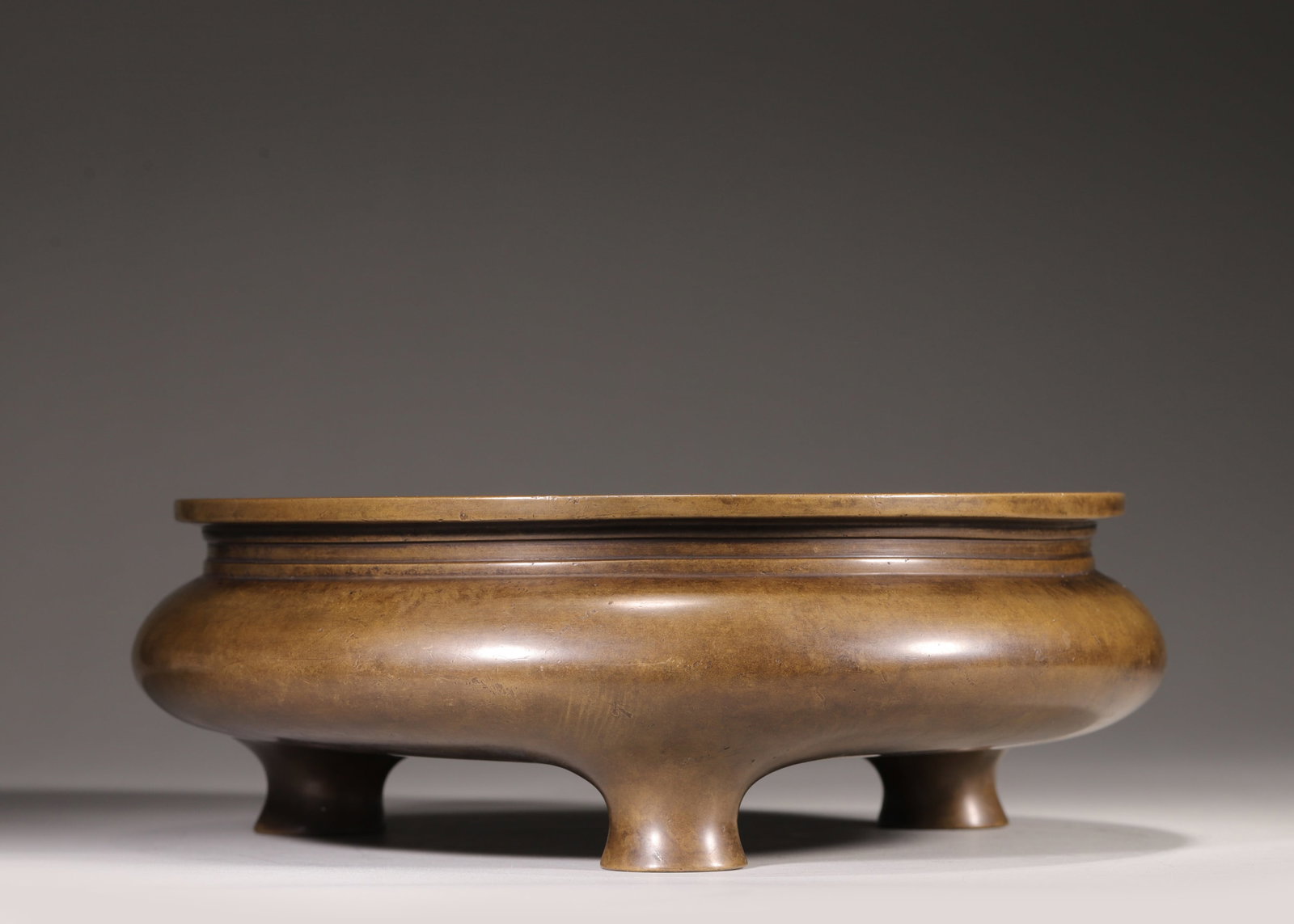 A Bronze Tripod Li-Style Censer, Marked "Xuan De Nian Zhi", Qing Dynasty: D 26.0cm (10.24 in); H 8.5cm (3.35 in); Wt 6056.0g (13.35 lb)A bronze tripod Li-style censer, marked "Xuan De Nian Zhi", Qing Dynasty. Made of solid refined bronze with warm patina, it features elegan