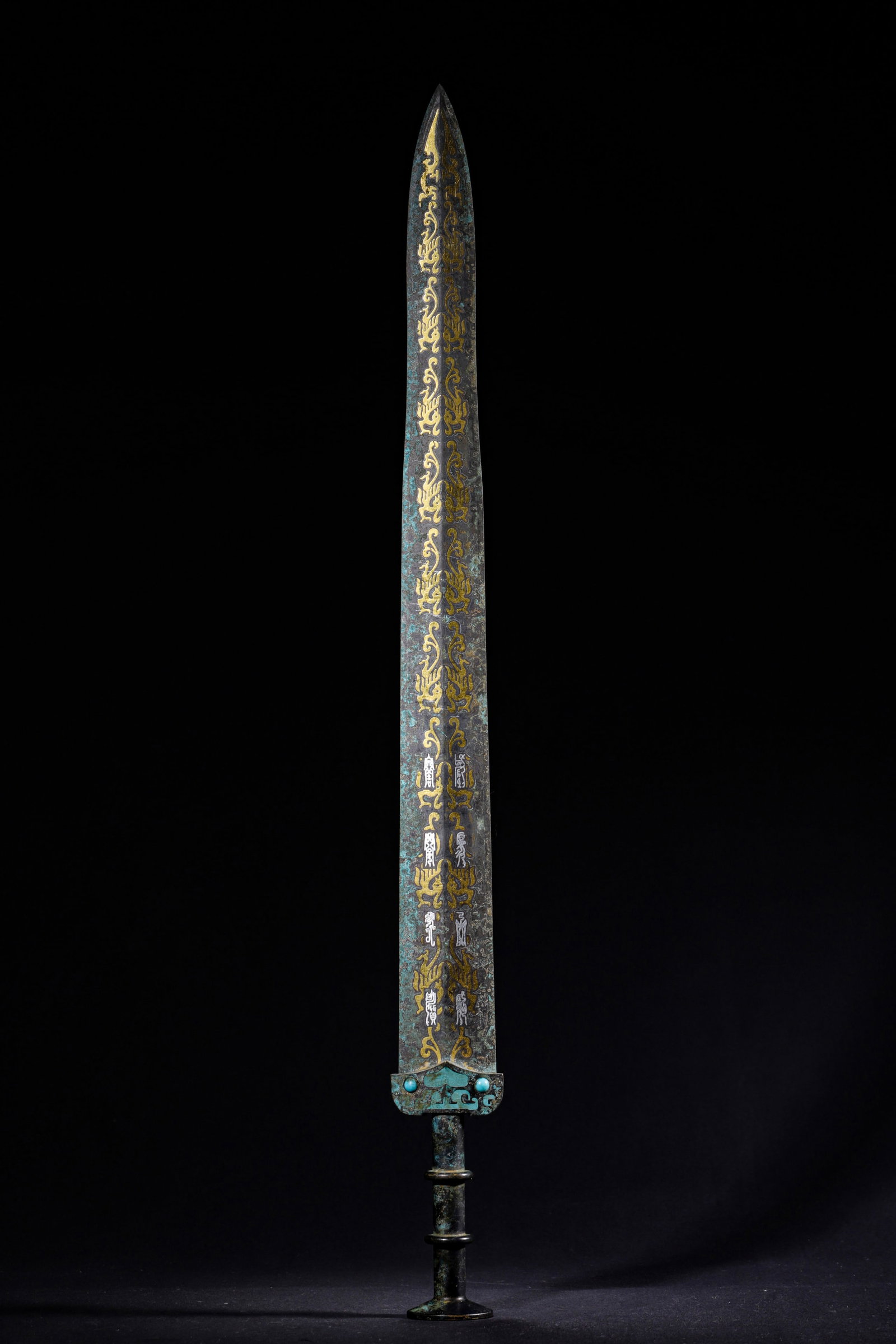 A BRONZE Ornament INLAID GOLD, SILVER, TURQUOISE AND EPIGRAPHS, WARRING STATES PERIOD: L 61.00cm (24.02 in); W 6.00cm (2.36 in); Wt 942.00g (2.08 lb),Standard bronze long Ornament with double-ring grip and round pommel, turquoise inlay on guard. Blade fully decorated with symmetrical go