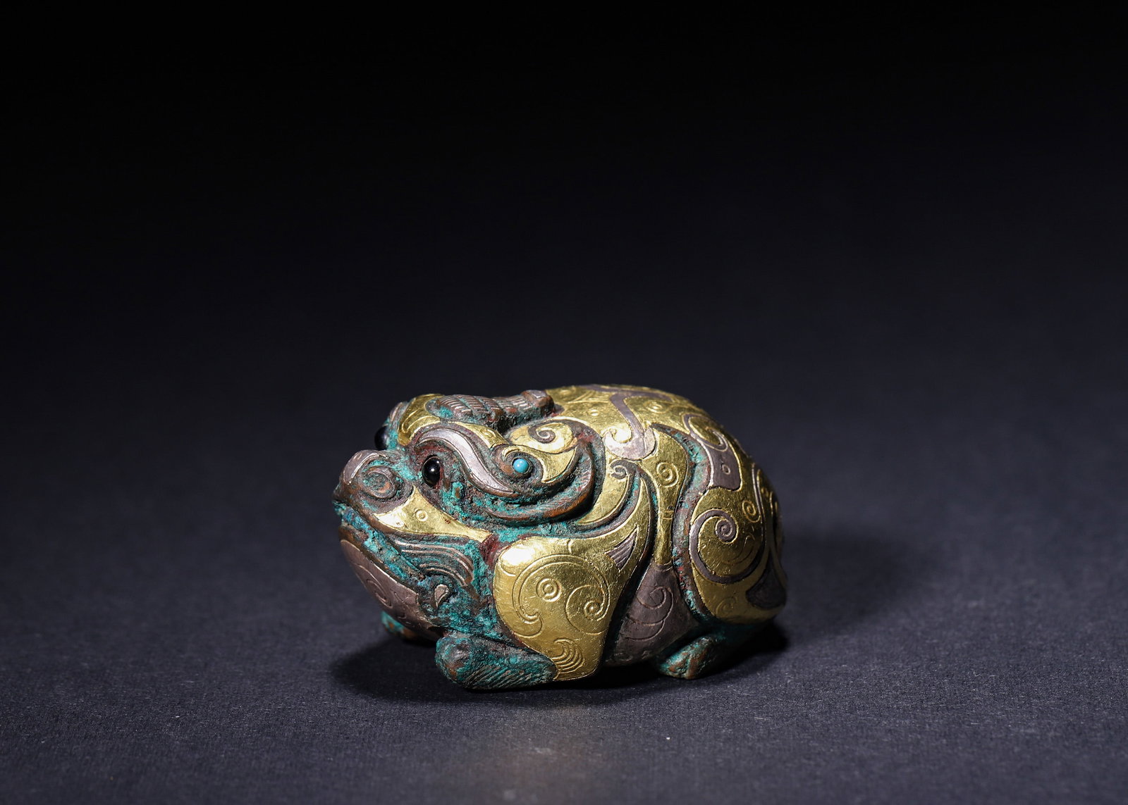 WARRING STATES PERIOD, BRONZE PAPER WEIGHT INLAID WITH GOLD, SILVER AND TURQUOISE IN FORM OF: L 4.70cm (1.85 in); W 3.60cm (1.42 in); H 2.60cm (1.02 in); Wt 99.00g (0.22 lb),Warring States bronze recumbent beast weight fully decorated with interlocking gold and silver spiral cloud patterns, in