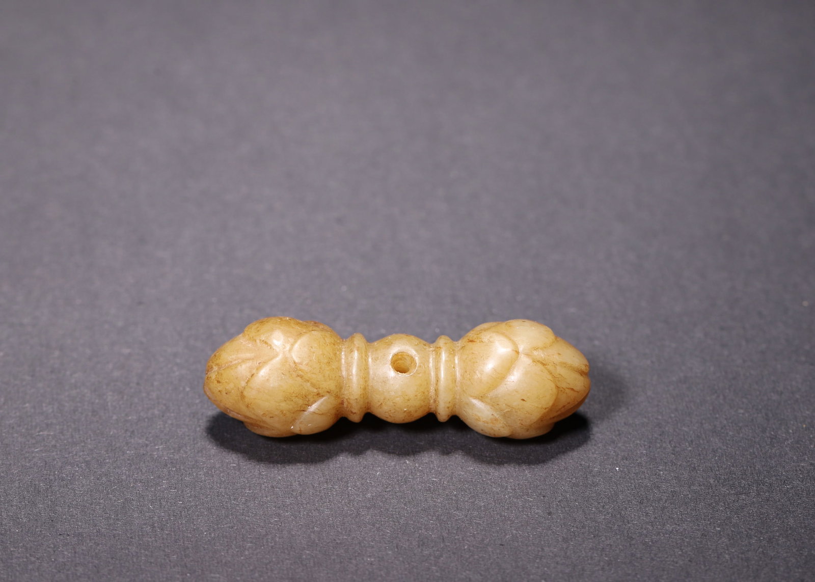 A Hetian Jade Lotus Vajra Pendant, Ming Dynasty: L 4.7cm (1.85 in); W 1.4cm (0.55 in); Wt 15.0g (0.03 lb)A Ming Dynasty pendant carved from Hetian jade with warm patina. Shaped like a vajra, it features symmetric lotus buds at both ends and a centra