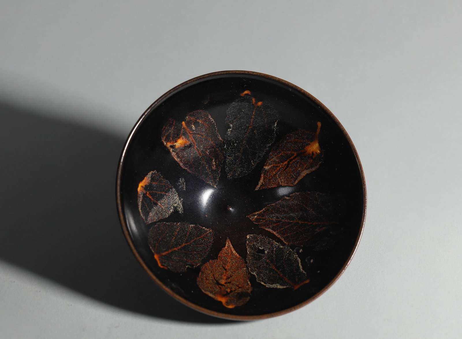 A Jizhou Kiln Black-Glazed Conical Bowl with Leaf Imprint Decoration, Song Dynasty: D 14.3cm (5.63 in); H 5.5cm (2.17 in)A precious Song Dynasty conical tea bowl from Jizhou Kiln with classic leaf-imprint craft. Glossy black glaze holds seven natural leaf patterns with clear veins ag