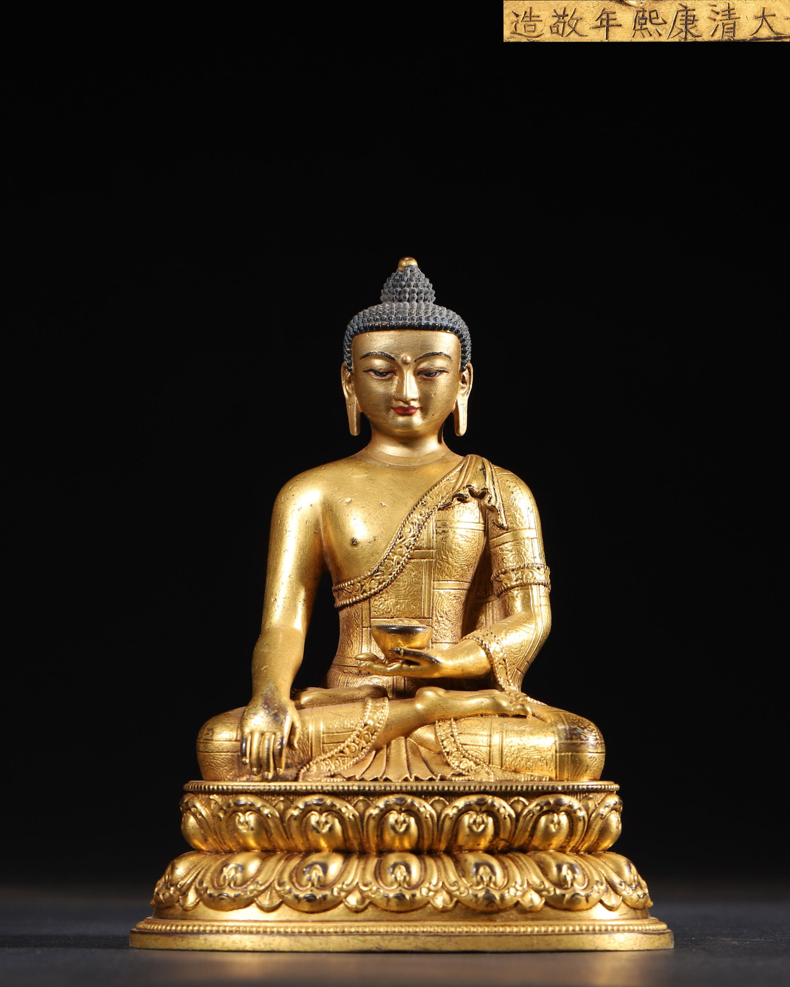 AN IMPERIAL GILT-BRONZE FIGURE OF SHAKYAMUNI BUDDHA, KANGXI PERIOD, QING DYNASTY: 3.35" x 4.72" x 6.3" inches (8.5 cm x 12.0 cm x 16.0 cm) | Weight: 1.64 lbs (745.0 g)An exceptional imperial masterpiece from the Kangxi court, bearing the inscription "Da Qing Kangxi Nian Jing Zao". 