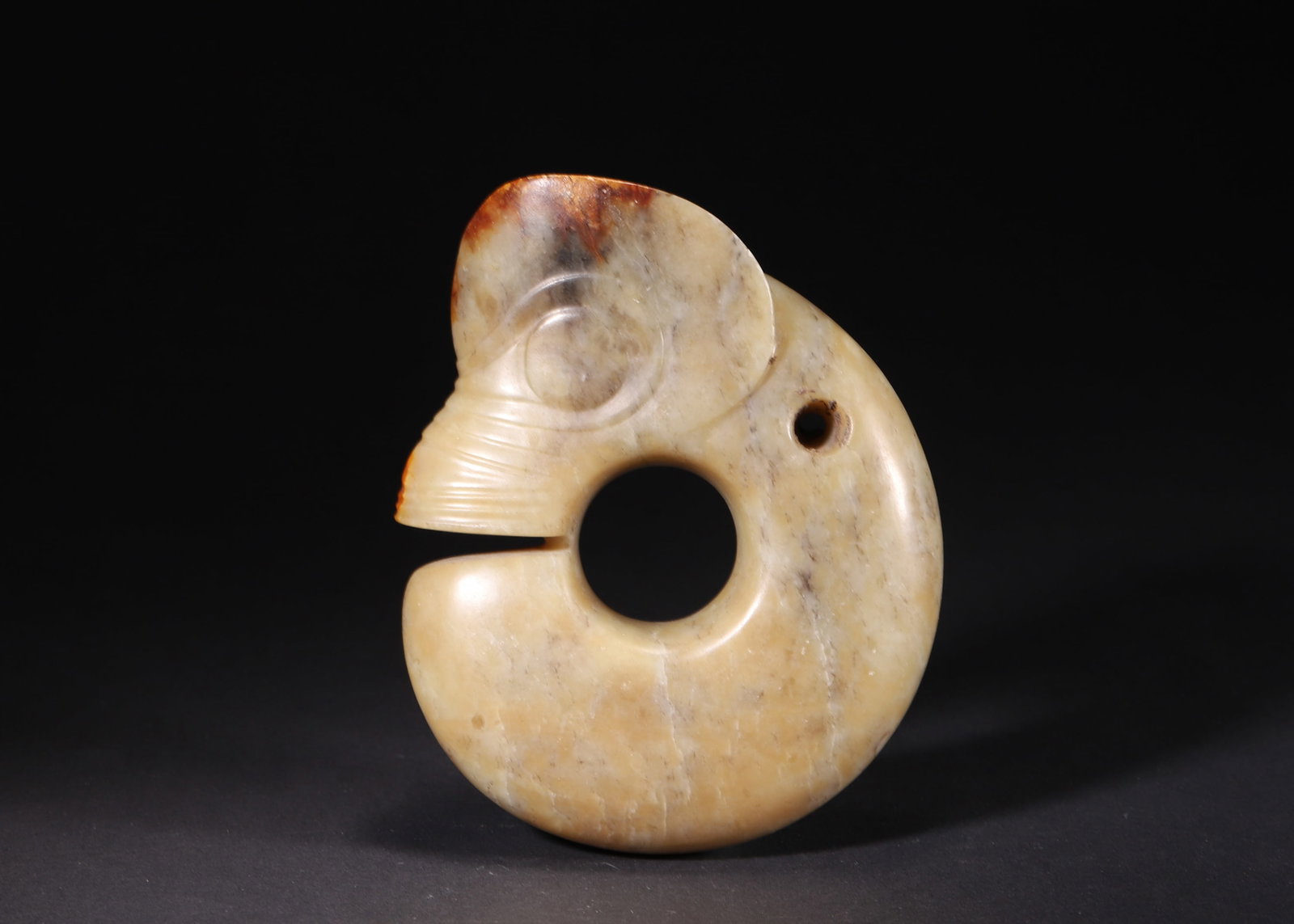 A Hongshan Culture Jade Pig Dragon, Neolithic Period: L 13.5cm (5.31 in); W 11.0cm (4.33 in); T 3.5cm (1.38 in); Wt 892.0g (1.97 lb)A Neolithic Hongshan Culture jade pig dragon. Carved in a coiled form with simple yet elegant lines, it features natural p