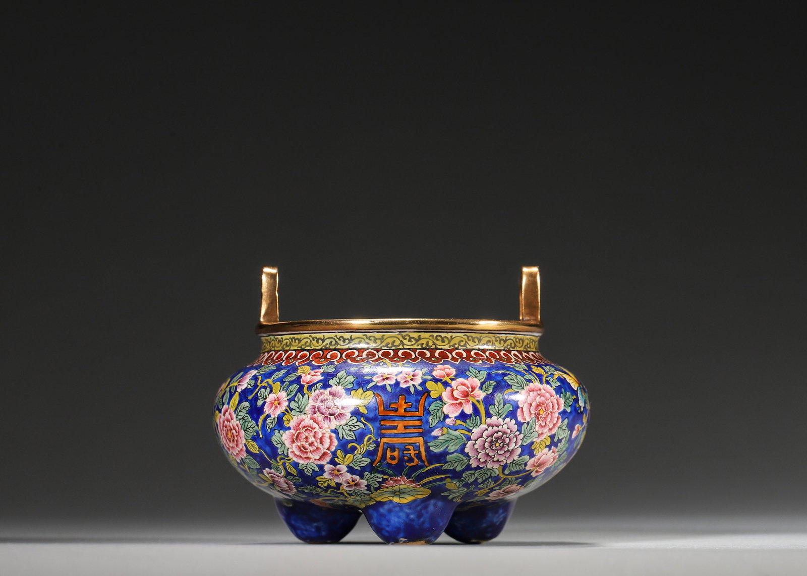 QIANLONG PERIOD, QING DYNASTY COPPER-BODIED ENAMEL TRIPOD CENSER WITH FLORAL AND LONGEVITY: 3.15in (8.0cm), 0.575lb (261.0g)A fine Qianlong period copper enamel tripod censer with gilt rim, bridge handles, and vibrant floral and longevity character motifs. Marked "Qianlong Nian Zhi", it exem