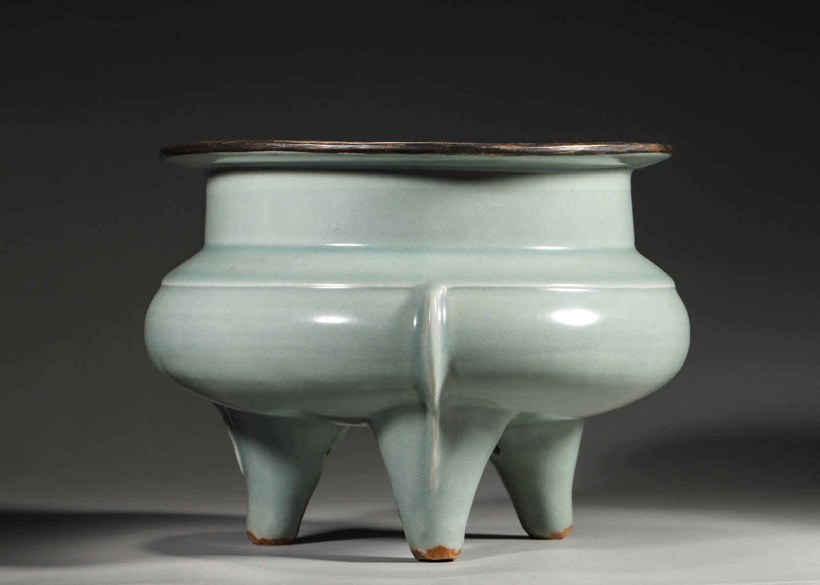 A Silver-Gilt Mounted Longquan Celadon Tripod Censer with "Huangji Dian" Mark (Song Dynasty): 26.0 x 26.0 x 19.0 cm (10.24 x 10.24 x 7.48 in)A Song Dynasty Longquan celadon tripod censer with silver-gilt rim and "Huangji Dian" mark. It features a soft, jade-like celadon glaze, embodying classi