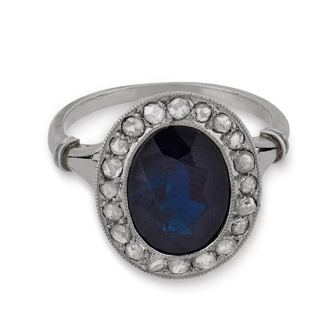 Sapphire and Diamond Halo Ring, White Gold / Platinum: SAPPHIRE AND DIAMOND HALO RING, WHITE GOLD / PLATINUM Description: The ring is centered on an oval-cut deep blue stone, likely a sapphire, exhibiting a rich tonal depth with subtle internal inclusions