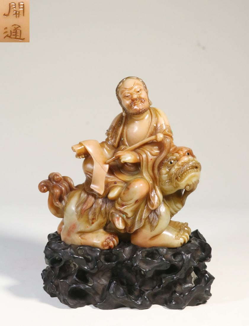 A Shoushan Furong Stone Lion-Riding Arhat Figure: A Shoushan Furong Stone Lion-Riding Arhat Figure. Dimensions: 7.09in x 5.59in x 2.60in Weight: 2.03lbs.