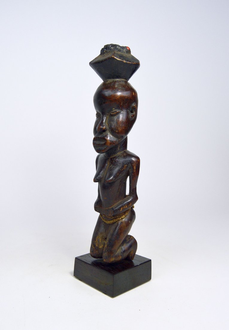 A Rare Suku magic fetish, African Art: A carved wooden female magic fetish with magic inserted on top and sealed with a mirror, resins and abruss seeds. The female is shown kneeling and has a well handled patina. Suku peoples, Congo, Afric
