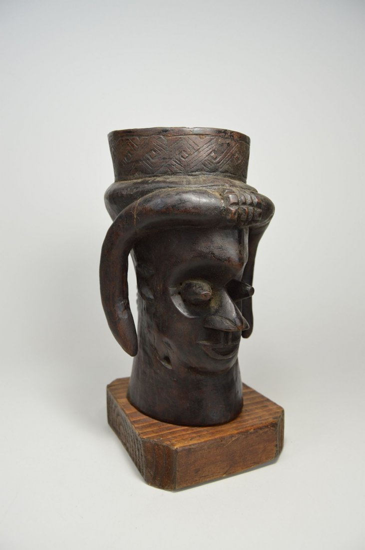 A Kuba palm wine cup with animal horns, African Art: A Vintage carved wooden beaker with ancestor face adorned with Ram like horns. Incised geometric designs and custom mounted to display stand. Kuba people, Congo, Africa. The cup measures 8.75 x 6.25 i