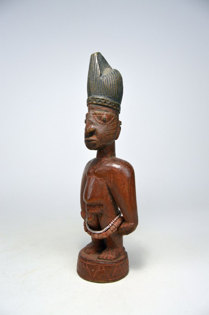 A Yoruba Ibeji twin idol, African Art: A carved wooden male idol with tall conical hat with incised designs, traditional facial scars, metal inset eyes and reddish patina with antique glass bead adornment. Yoruba peoples, Nigeria, Africa.