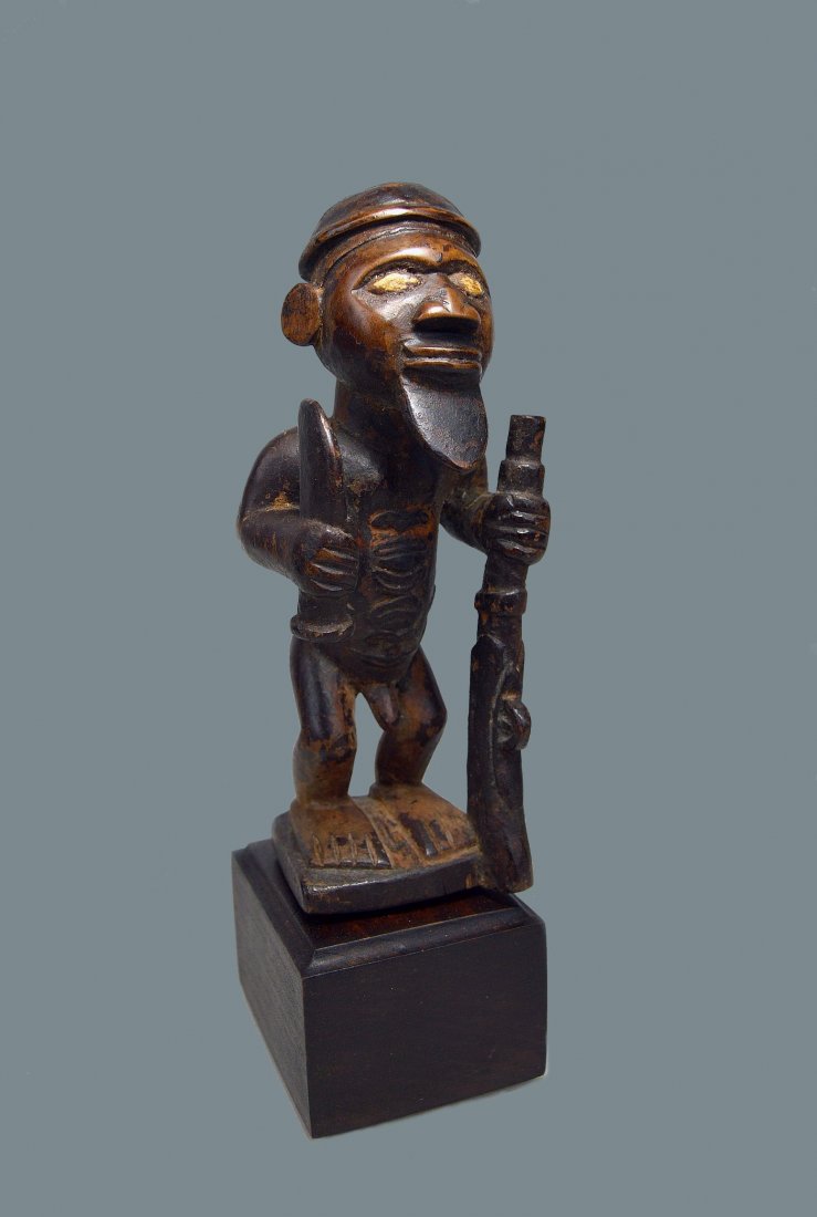 A Fine Bembe Male Ancestor sculpture African Art: A very finely crafted vintage male sculpture with raised tribal scars on the abdomen, a ceremonial cap, and shown holding a rifle and a sword. With inlaid bone(?) eyes. Bembe peoples, DRC/Congo, centr