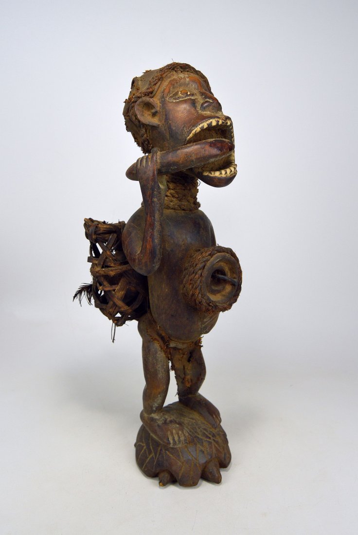 Kongo style fetish chewing Iboga Root, African Art: Carved wooden Kongo style fetish showing a ancestor standing on a tortoise and wearing a rattan pack filled with magic substances as he chews on the Iboga root. Measures 21 inches tall. Ex Harold Smit