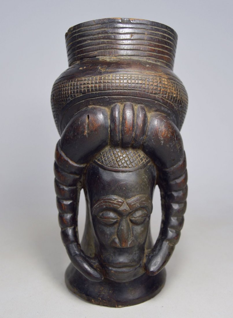 FINELY CARVED KUBA PALM WINE CUP: A finely crafted carved wooden beaker with stylized ancestor face and ram horns. Kuba peoples, Congo, Africa. The Cup measures 9 x 5 inches.