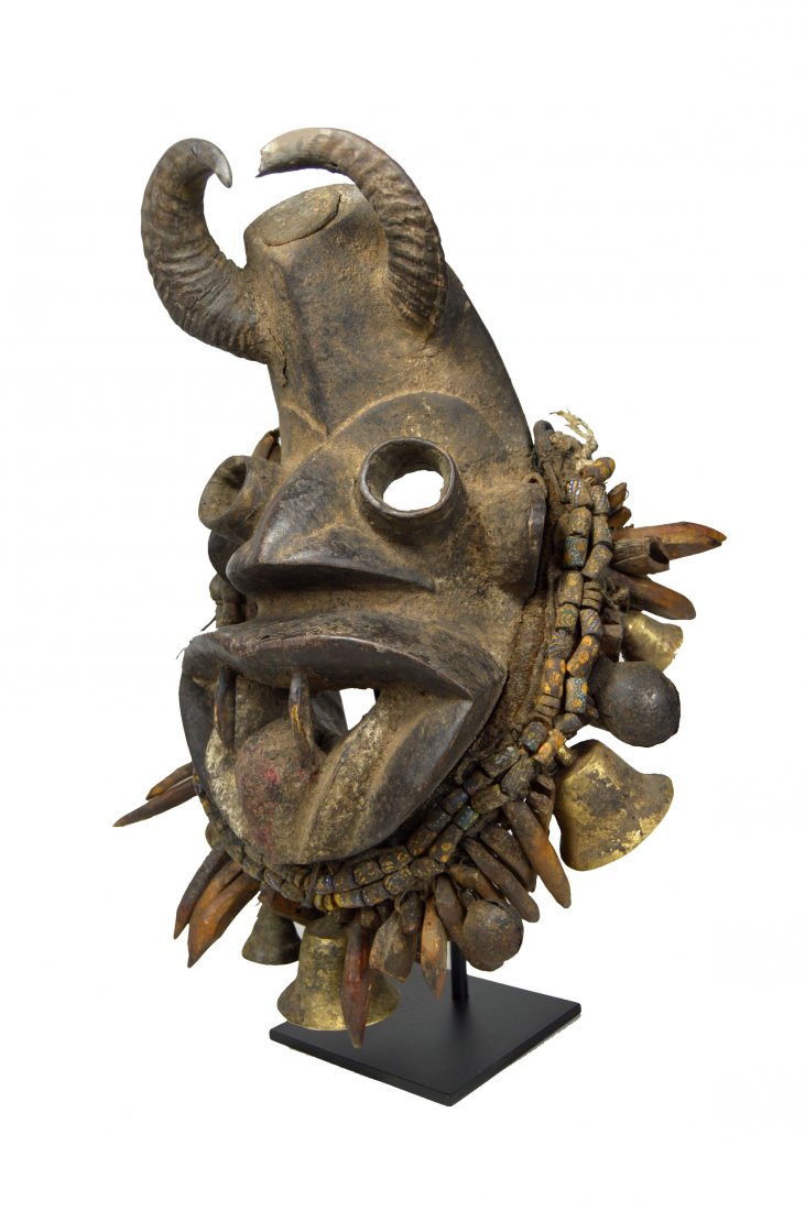 Fierce Dan Guere Mask with Bells, beads and Animal Horn: A fantastic and highly stylized carved wooden mask with fierce facial treatment, wide open tubular eyes, wide open mouth with animal teeth and a full regalia of bronze bells, old millefiori trade bead