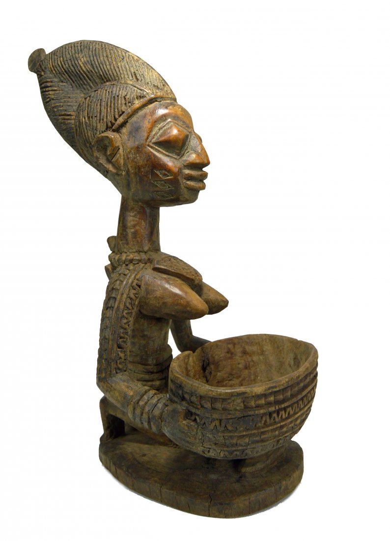 A Fine Yoruba Offering Bowl with Kneeling Female: A Finely carved wooden female with offering bodl effigy , featuring elaborate incised and raised design and traditional style. Yoruba peoples, Nigeria, Africa. The figure measures 14 inches tall x 10 