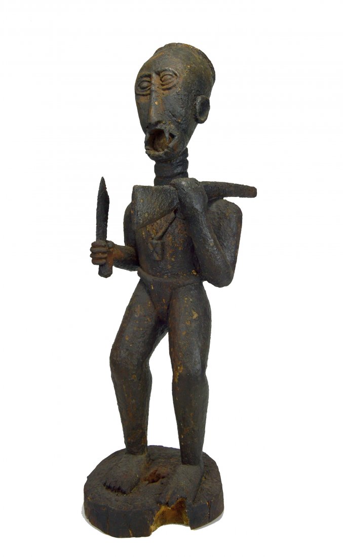 A Baule Magic Fetish Ex Allan Stone Collection: A Tall carved wooden fetish figure with large gaping mouth and long fangs, heavily encrusted surface and shown holding a sword and rifle.Carved wood; 32" x 10" x 11 1/2"; Provenance: Michael Oliver, N