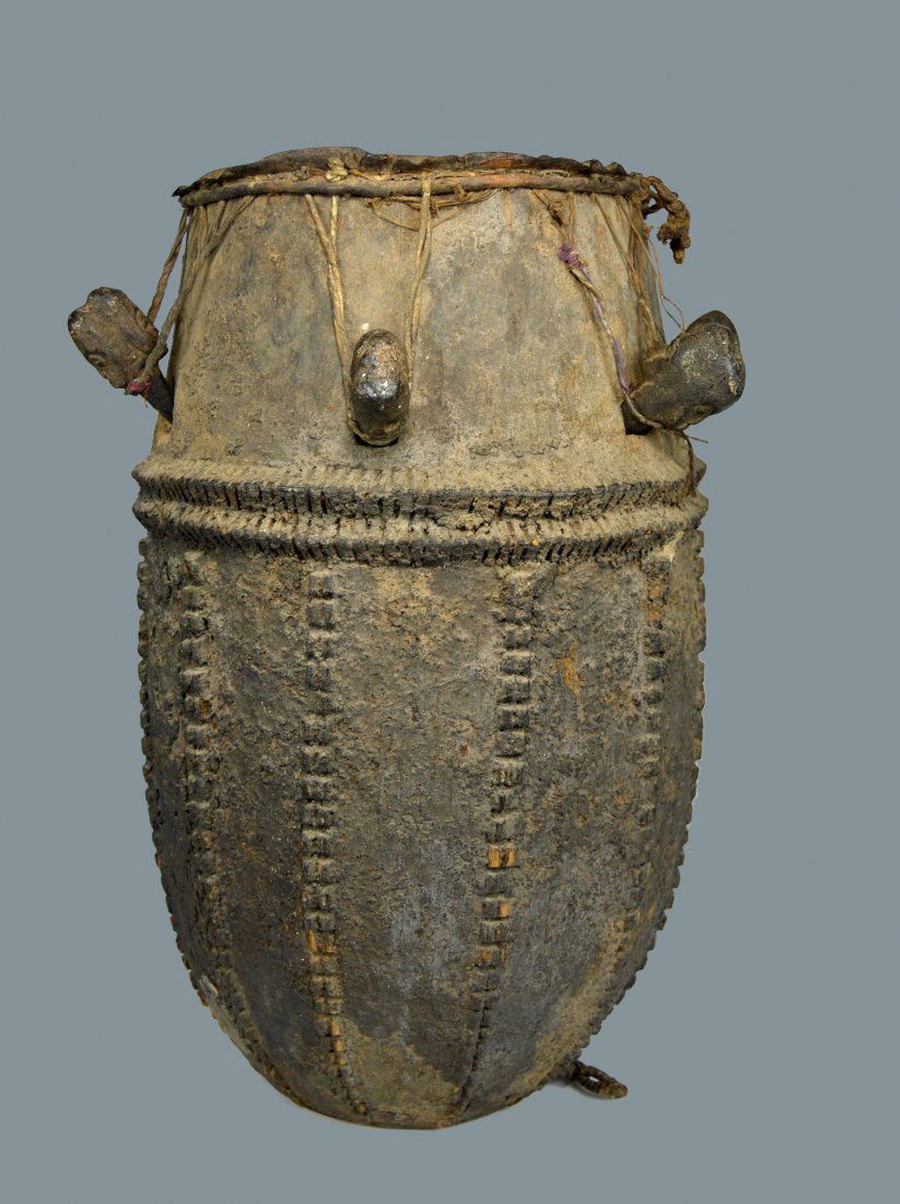 Old Carved Wooden Drum From the Baule Peoples: This is a very old and field used tribal drum with raised designs, carved wooden pegs with mask faces and obvious age and use over many years. The Drum measures 22 x 16 inches ( the drum head is 11 in