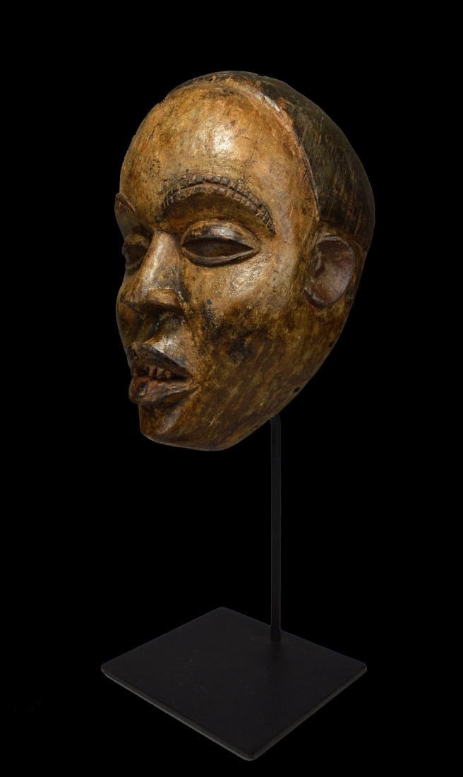 A Bakongo African Mask on custom base: A carved wooden dance mask with realistic style face, carved filed teeth and protruding tongue. Bakongo peoples, DRC / Congo, Africa. The mask itself measures 12.5 x 7.5 inches ( 19.5 inches tall on p