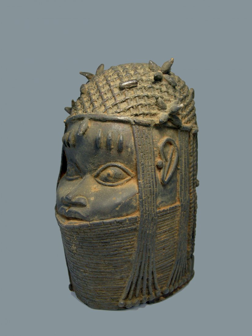 Benin Memorial Bronze Head of an Oba: This is a commemorative cast-brass sculpture depicting the idealized likeness of an oba, or king, wearing a woven cap of coral beads, with lateral strands of coral suspended around both ears. A single