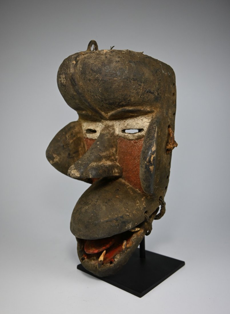 A Dan Kran African Mask: A Carved wooden mask with retractable lower jaw, embedded with bone or animal teeth , and accented with mineral pigments. Kran ethnic group, Dan complex of tribes, Ivory Coast, West Africa. A metal di