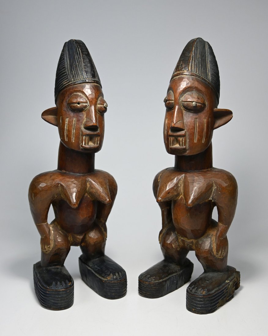 A Fine Pair of Yoruba Ibeji Twin Idols: A very finely carved pair of female twin idols with incised scar designs accented with kaolin clay, inset nails as pupils, dyed coiffure, raised sandals and a obviously well handled and deeply patinat