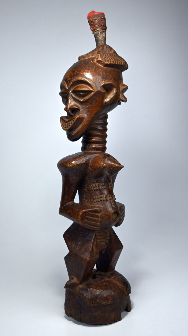 A Songye female Sculpture: Carved from a very heavy and dense wood with highly exaggerated features and form, note the head turned off axis and embellished with Magic fetish Horn, copper wire, raised scar designs and a polished