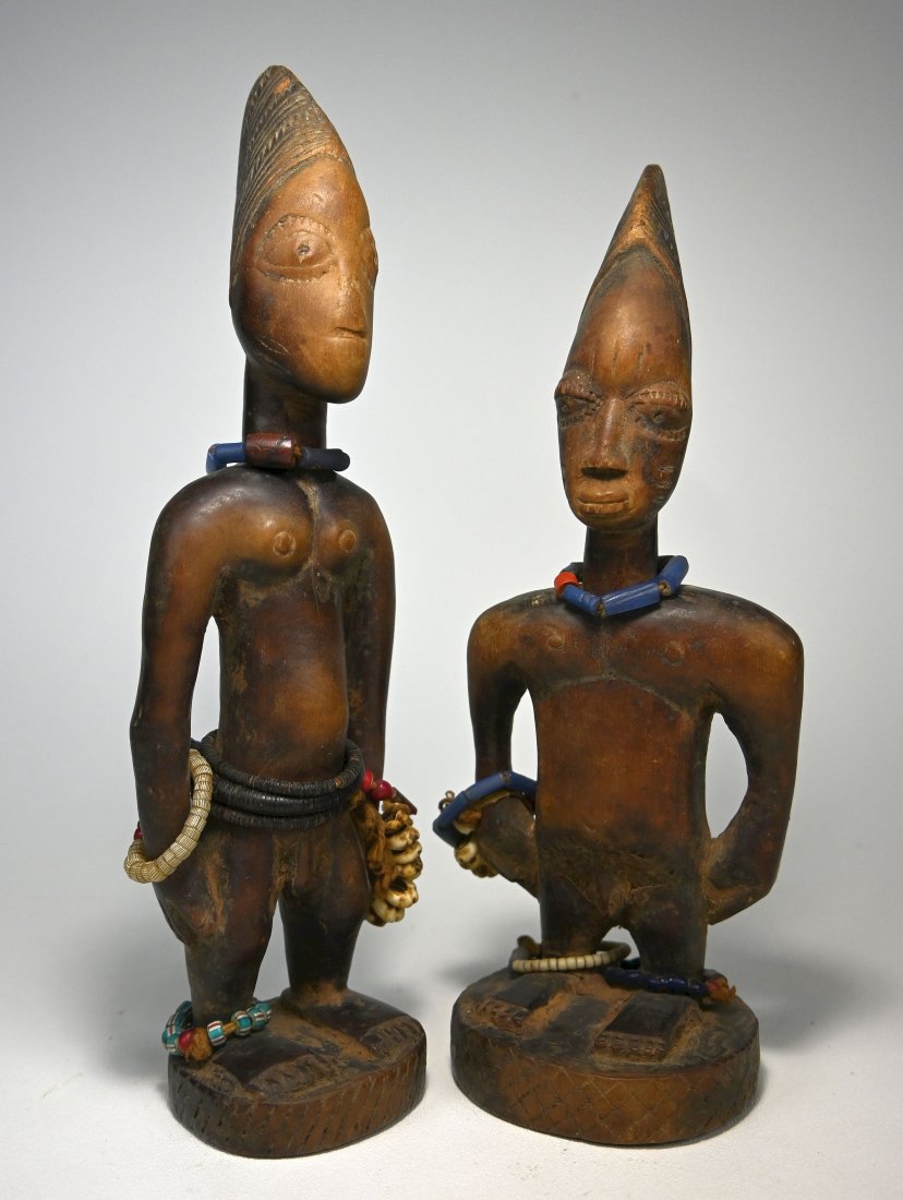 A Pair of Yoruba Ibeji Male Twin Idols: A carved wooden pair of male twin effigies with deep well handled surface patina and embellished with cowrie shells and old glass beads. These figures, known as ere ibeji and are considered mediums to