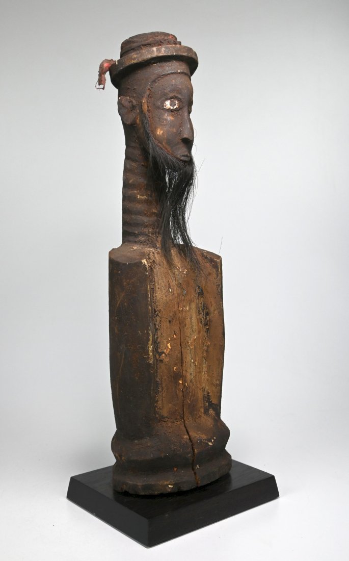 Rare Bidjogo Iran Otibago Ancestor shrine Idol Ex Banks: A carved wooden shrine object with tall slender ringed neck, carved face and top hat, embellished with animal hide beard, red textile and encrusted surface. To the Bidjogo peoples, the spirits of the 