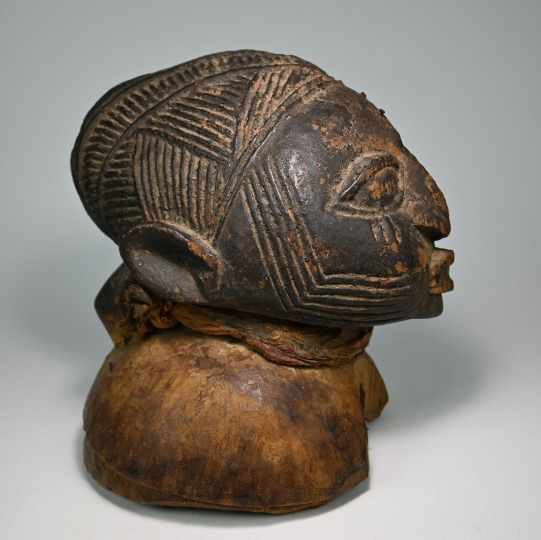 A Yoruba Egungun Helmet Mask: A very old well used carved wooden Egungun cap mask with old textiles, nails and signs of field use. The mask was carved from a heavy dense wood. Yoruba peoples, Nigeria. The mask measures. Provenance