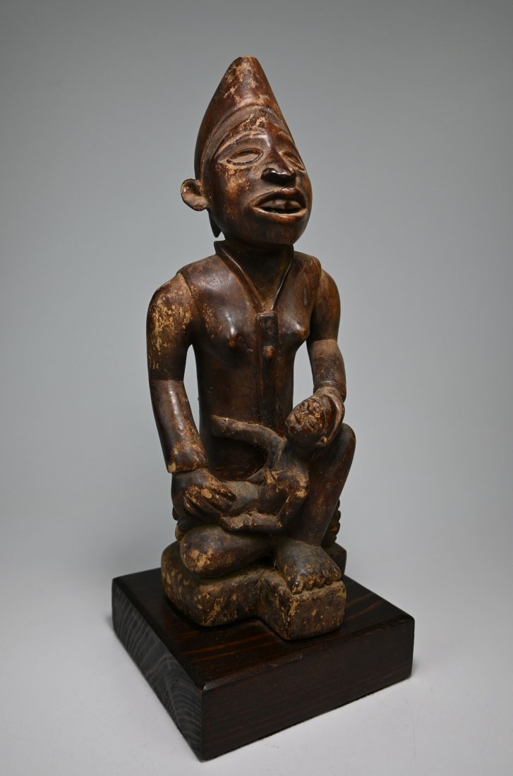 Yombe Phemba Maternity Sculpture Ex Jack Oliver, France: A carved wooden effigy of a mother and child wearing a ritual cap and what appears as a colonial era shirt, carved teeth and well handled surface patina. Traditionally phemba are used to symbolise the