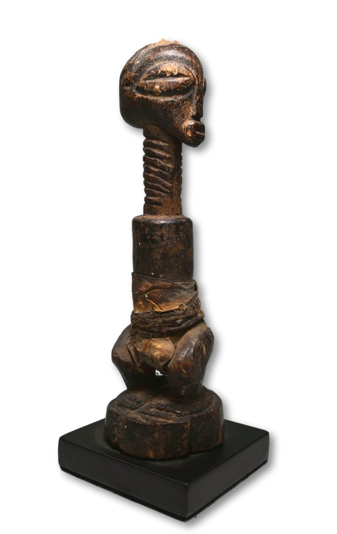 A Songye Shrine Idol: A Carved wooden effigy with head turned off axis, exaggerated form with no arms and embellished with a leather hide wrap. Songye peoples, DRC/ Congo, central Africa. Measures 7 inches tall ( 7.5 inche
