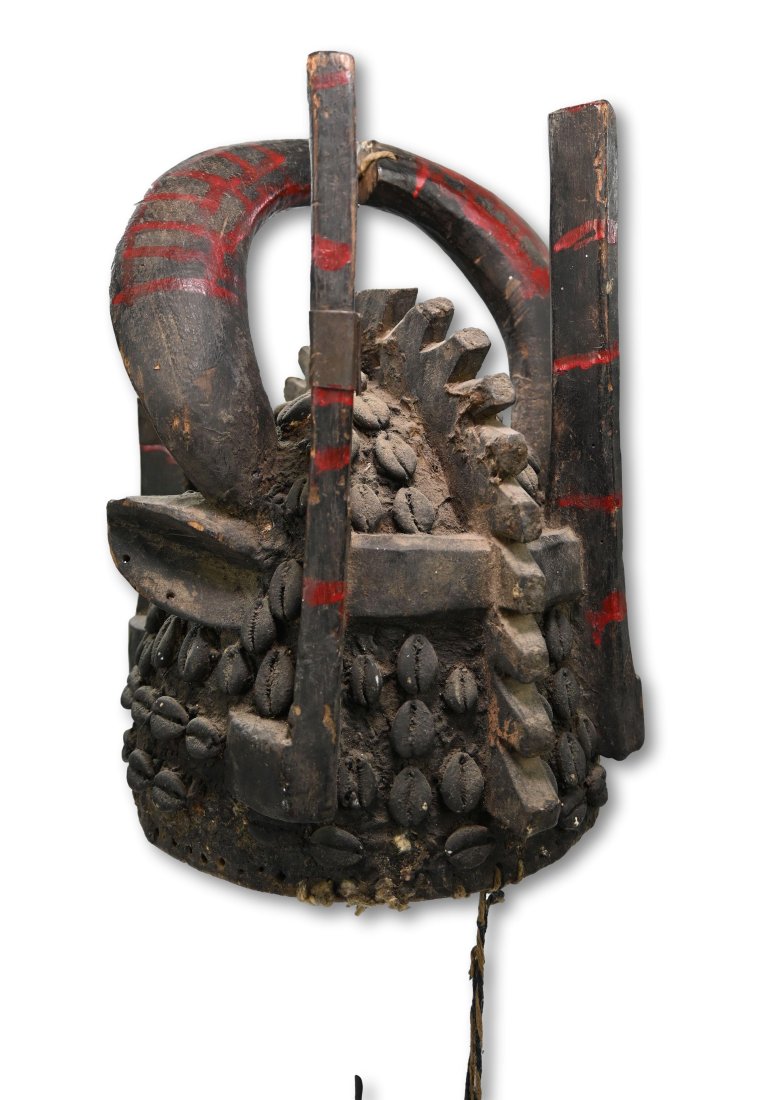 A Painted Senufo Helmet Mask: A carved wooden hat like dance crest or helmet of hollowed domed form, perforated around the edges for attachments, a raised serrated ridge dividing the top with a pair of ears below two horns which c
