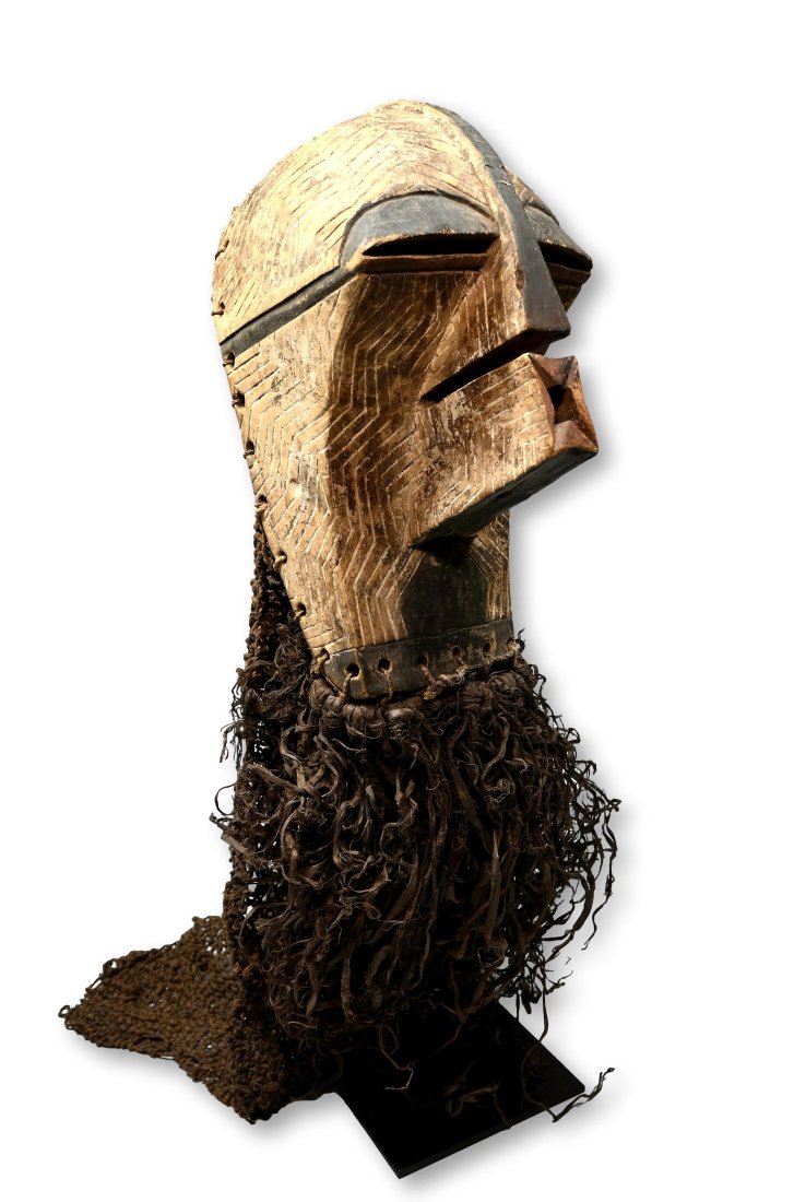 A Songye Kifwebe Female Dance Mask Ex Hautelet Collection: A carved wooden helmet mask featuring traditional incised linear designs, stylized protruding mouth and facial features with attached raffia headdress and collar. Songye peoples, Kifwebe society, DRC/