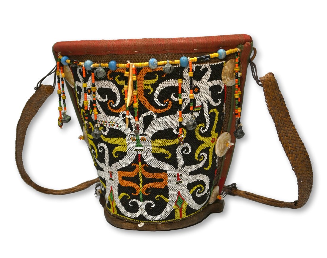 A Dayak Beaded Baby Carrier Basket Collected Prior to 1984: A highly decorated woven basketry and wood base basket adorned with an elaborate beaded panel with stylized naga / Dragons and sun like faces, bronze bells, teeth and old glass beads. Dayak peoples, B