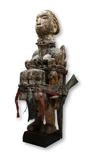 Published: Monumental Fon Vodoun Shrine Fetish Ex Simmons: A large and heavily embellished wooden female effigy with a large medicine bottle adhered to the front and two crocodile carvings attached to her form with red cloth, animal horns filled with magic in