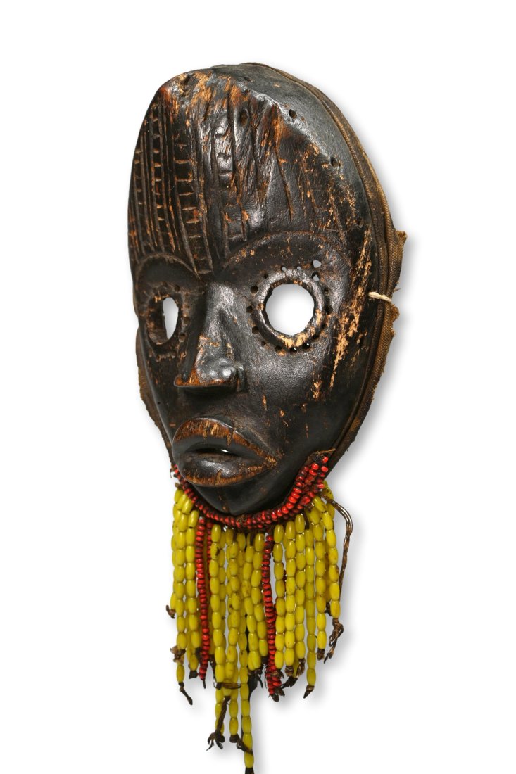 A Dan African Mask: A Carved wooden dance mask with well handled and worn surface, worn smooth incised linear designs and embellished with a beard made from glass beads. Dan peoples, Ivory Coast, West Africa. The Mask me