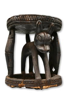 A Bamileke Stool with Hyena and Gong designs: A large carved wooden stool with a stylized Hyena as the central support and double Gong or Gogo bell designs on the outer edges, linear designs throughout. Bamileke peoples, Cameroon Grasslands, West