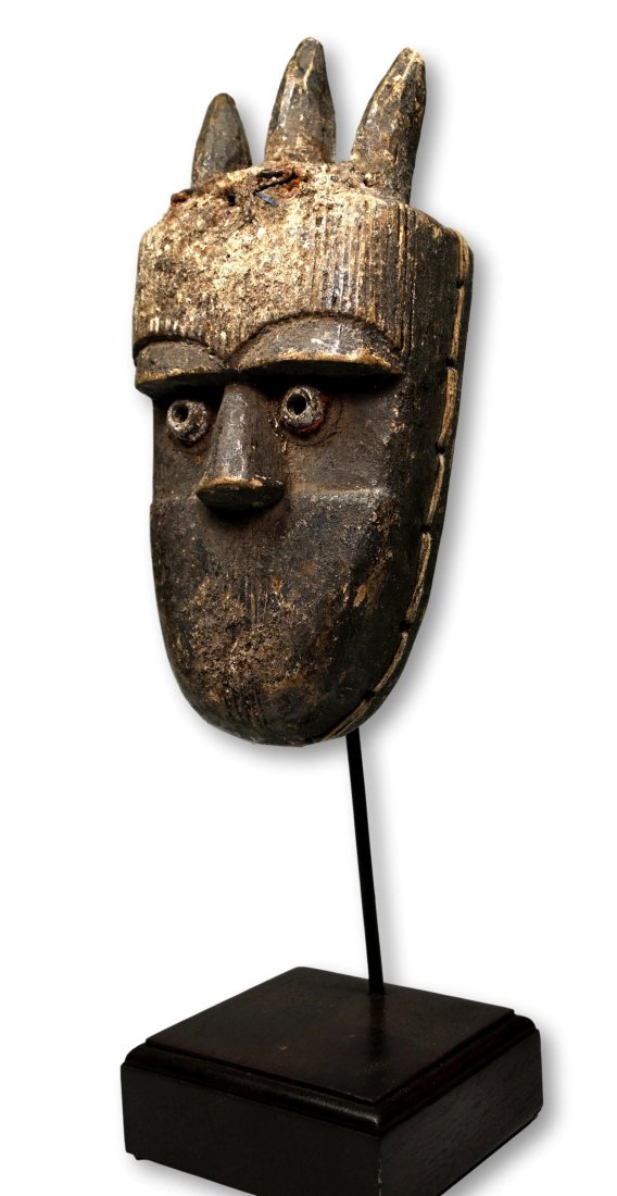A Toma African mask Ex Dr Jackson Collection: A small carved wooden mask with raised tubular eyes, three horns, linear designs and a encrusted surface. Toma peoples, Guinea or liberia, West Africa. The mask measures 12 x 5.5 inches, on custom bas