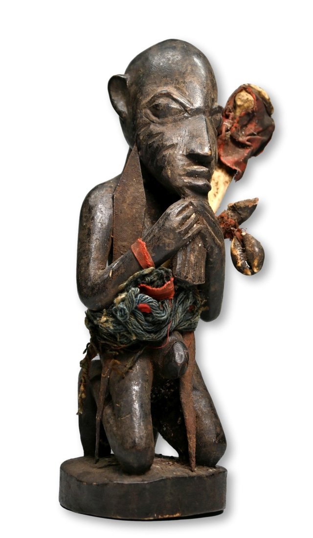 A Yoruba Orisha Magic fetish Sculpture Ex Dr Endicott Collection: A carved wooden male shrine idol with classic facial features, carved scar designs, shown holding his beard,and embellished with various iron spears, bones, shells and red textiles. Kneeling figures, 