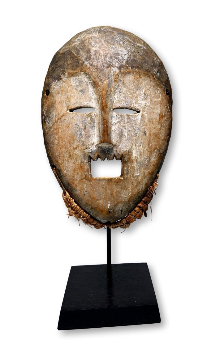 A Kumu African Mask Ex Banks Collection: A carved wooden ceremonial mask with aggressive open mouth with jagged teeth and embellished with kaolin clay pigments and raffia grass. Kumu peoples, DRC/ Congo, central Africa. The mask measures 10 