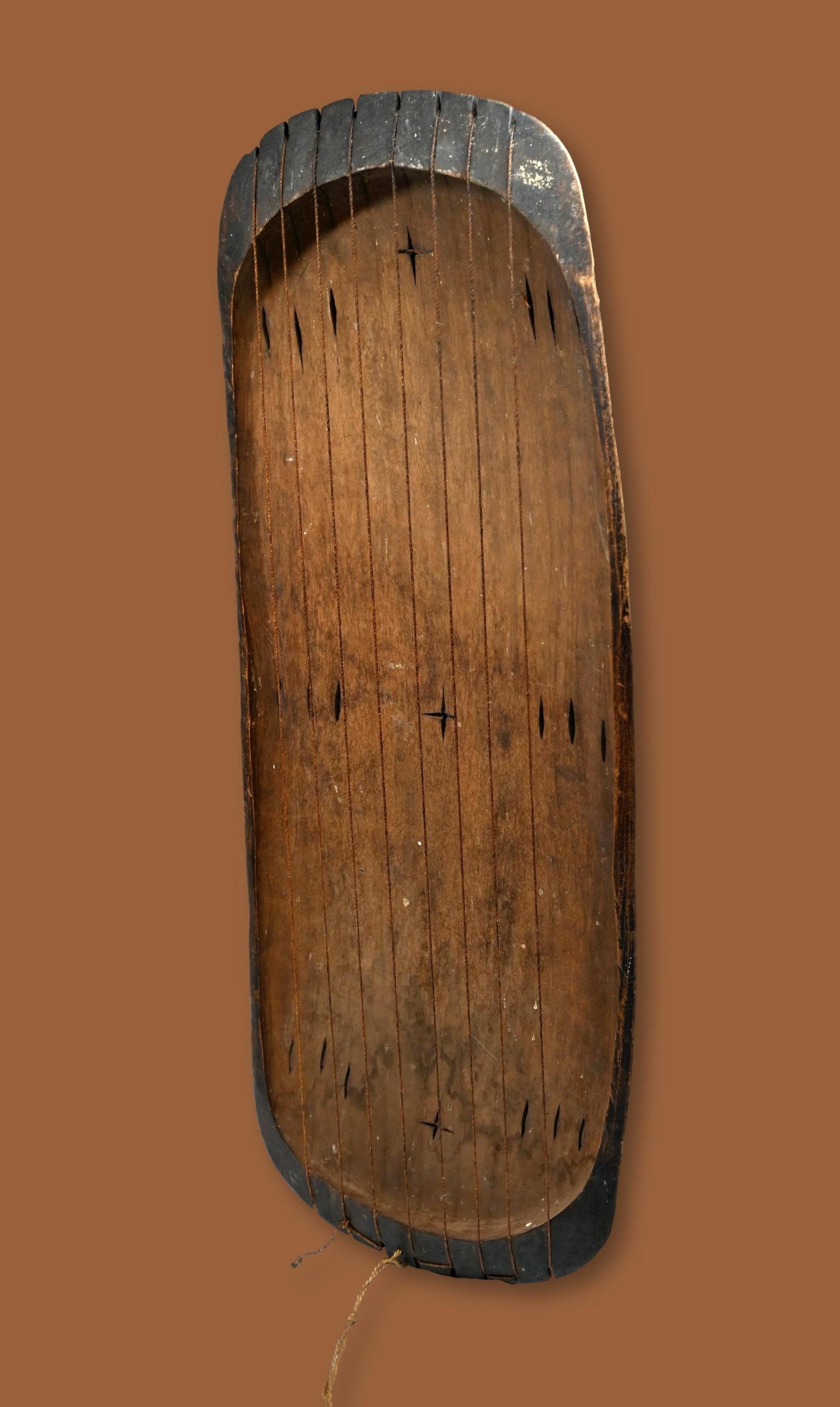 A Inanga Harp from Burundi: A large carved wooden musical instrument with hollowed out body, incised and decorated rim and several strings. In Burundi, the inÄnga was traditionally played for the mwamis of Burundi as they reste
