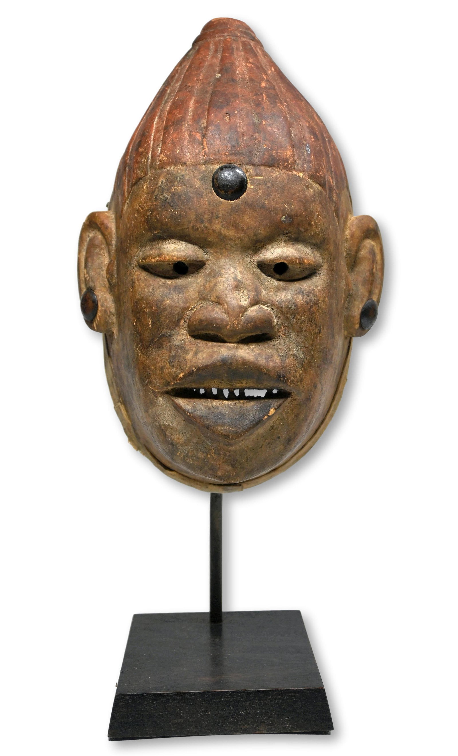 A Makonde Mask: A carved wooden dance mask with traditional filed and sharp looking teeth and a red mineral accented coiffure, and with metal studs in the forehead and as earrings. Makonde peoples, Mozambique, Africa
