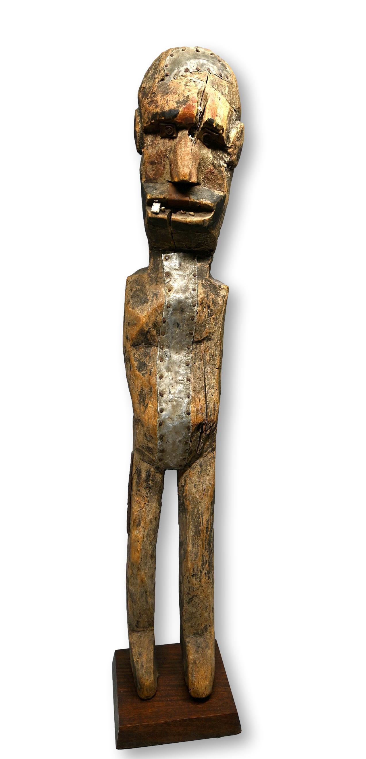 A Sukuma Shrine Idol Ex Simmons Collection: A Carved wooden spirit effigy with inset wooden teeth and painted designs. The sculpture is well weathered and worn and has metal repairs to stress fractures suggesting field use. Sukuma peoples, Tanz