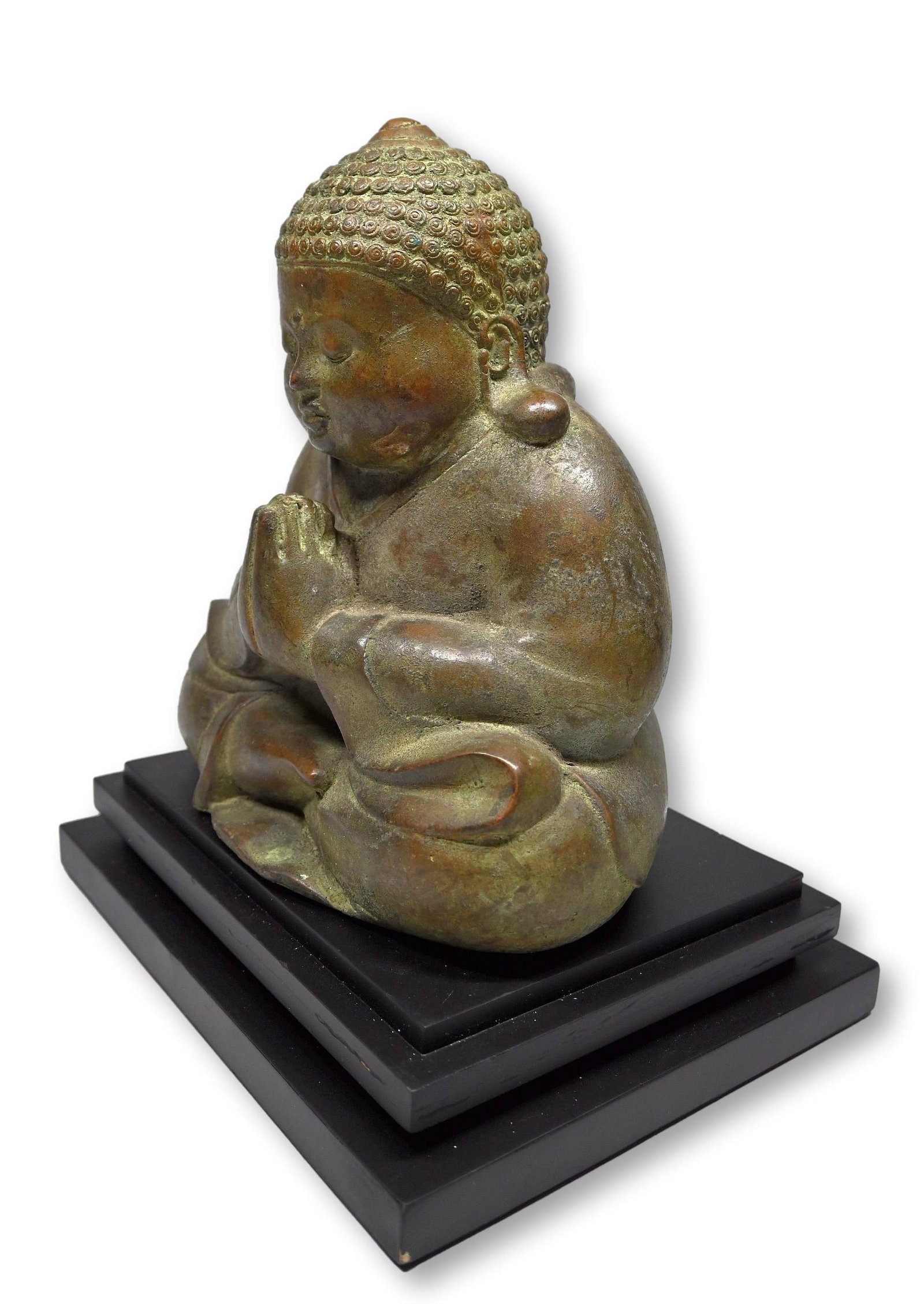 A Serene Balinese Bronze Buddhist Sculpture: Cast bronze Buddha with hands in prayer like pose, custom mounted to a display stand. The Buddha measures 12 x 10 inches. Bali, Indonesia.