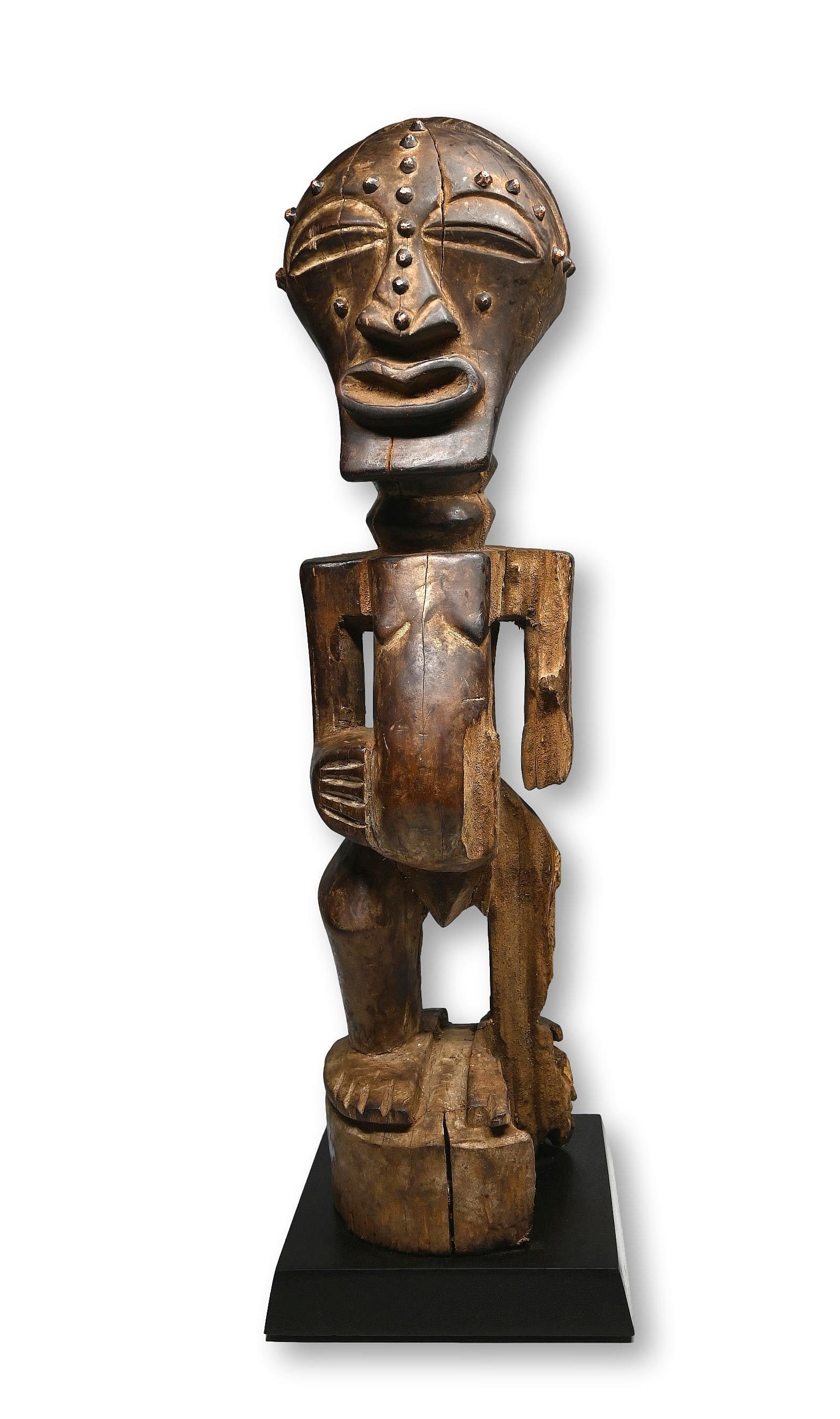 A Songye Nkisi Sculpture: A carved wooden male shrine sculpture with embedded brass tacks and well weathered surface. Songye peoples, DRC/ Congo, Africa. The sculpture measures 19 inches tall on its custom display stand.