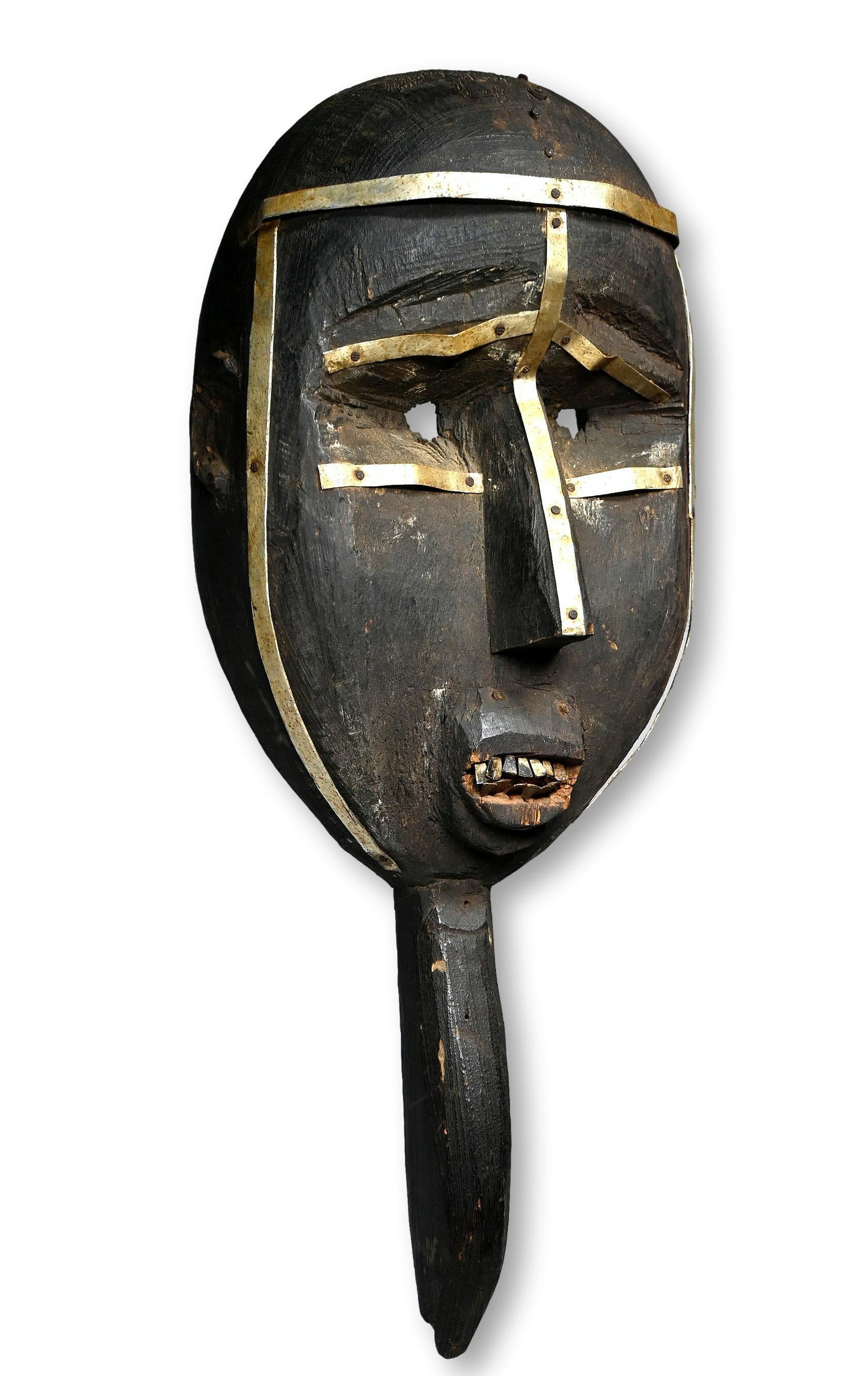 A Toma Ceremonial Mask: A Carved wooden ceremonial mask with a well handled and weathered surface, painted black and embellished with hammered metal work design, inset metal teeth and a bird like beak on the chin, similar to