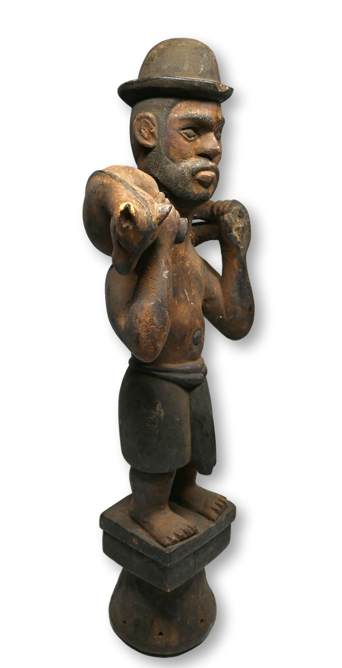 A Ibibio Dance Crest of a Hunter: A carved wooden dance crest sculpture featuring a Hunter carrying his game , with a top hat and pants, the male hunter has a beard and a wonderful folk art style. Ibibio or prerhaps Ogoni peoples, Nig
